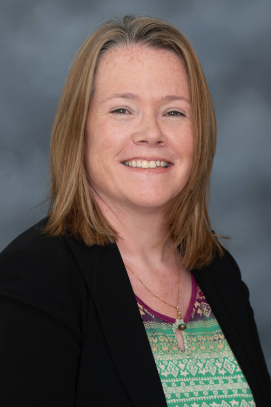 portrait photo of brunette woman wearing a green and blue shirt with a black cardigan